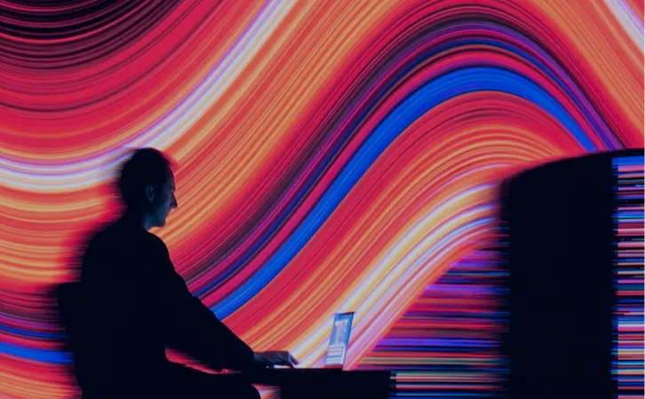 A person silhouetted against a screen of bright colour trails